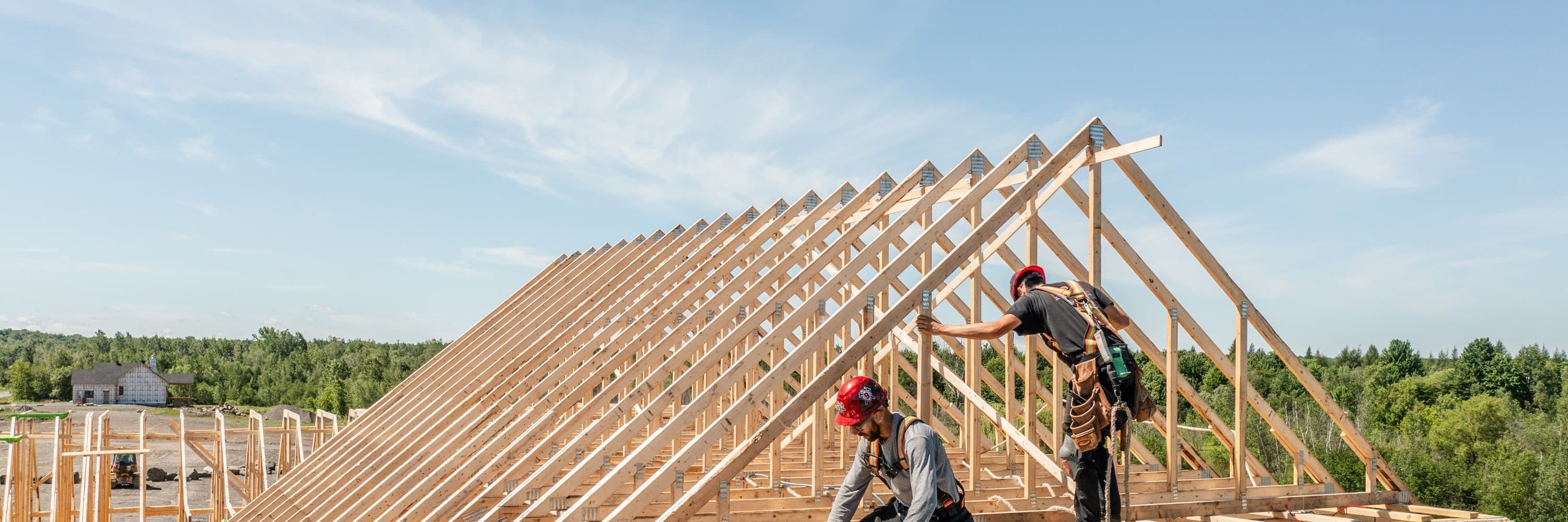 Deux charpentiers de l'équipe Clément Robert sur les fermes de toit d'une maison en construction